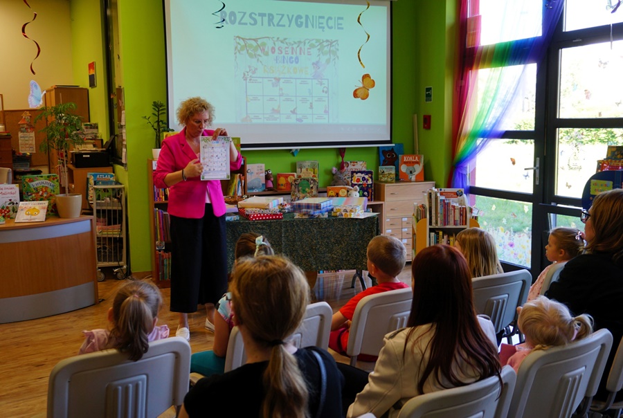 bibliotekarka stojąca przed zebraną publicznością pokazuje blankiet, do którego bingo używano w trakcie konkursu