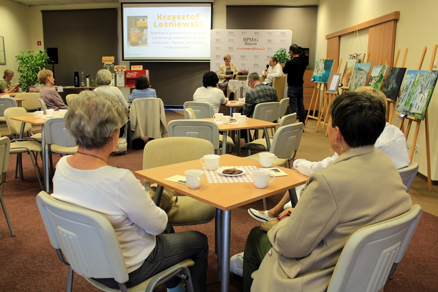 widzowie siedzą przy stolikach z kawą i herbatą, słuchają rozmowy prowadzonej z autorem