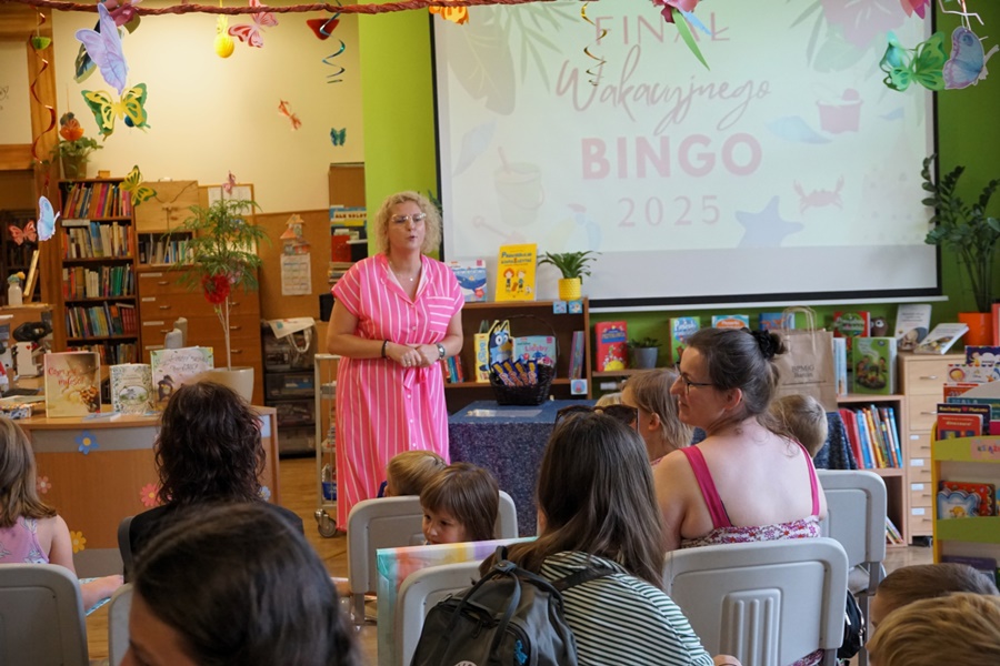 bibliotekarka rozpoczyna spotkanie, stoi przez zebranymi uczestnikami którzy siedzą na krzesłach