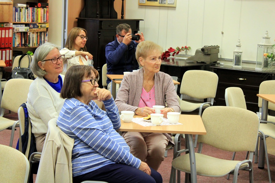 widzowie siedzą przy stolikach z kawą i herbatą, słuchają rozmowy prowadzonej z autorem
