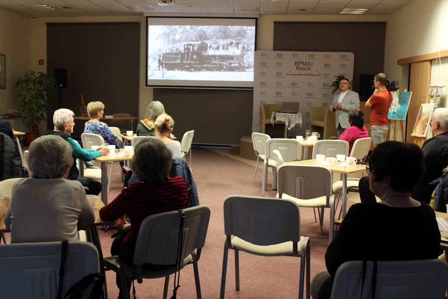 widownia siedząca na krzesłach przy stolikach słucha zaproszonego gościa