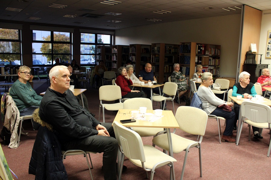 widownia siedząca na krzesłach przy stolikach słucha zaproszonego gościa