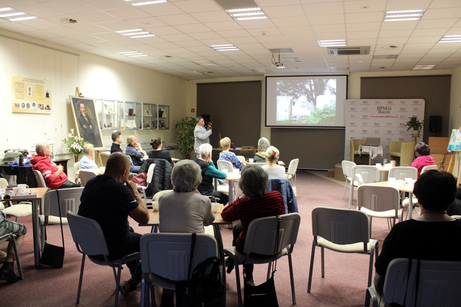 widownia siedząca na krzesłach przy stolikach słucha zaproszonego gościa