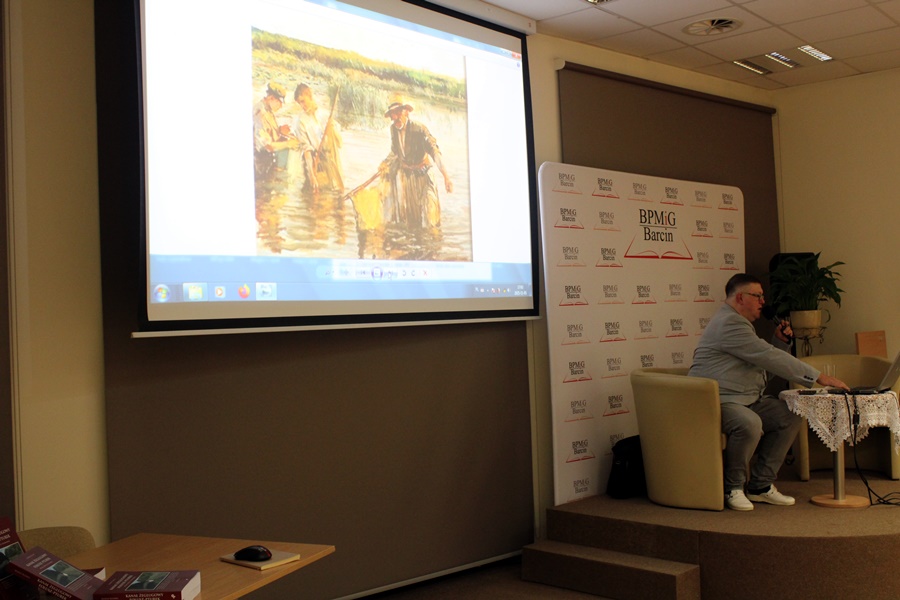 Zaproszony gość siedzi na scenie przy laptopie i wyświetla przez projektor zdjęcia o których opowiada