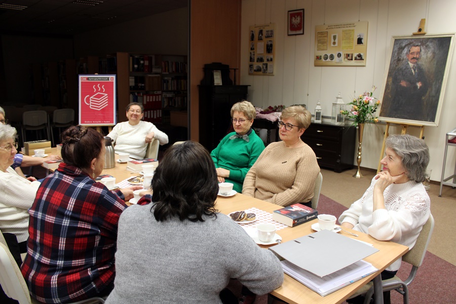 Osoby obecne na spotkaniu siedzą przy stole i dyskutują o przeczytanej książce.