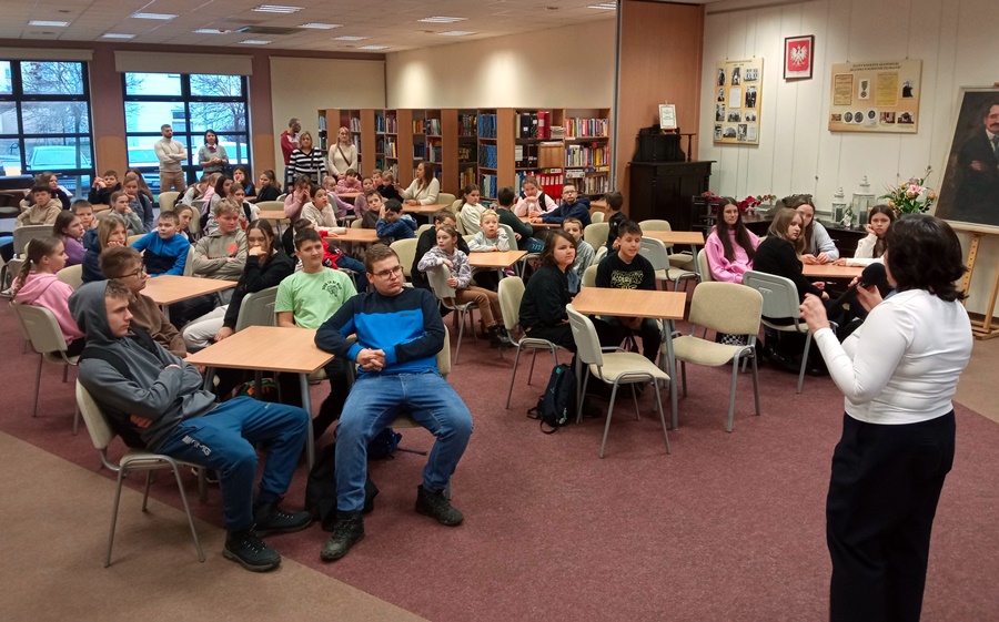 Odwiedzający zgromadzeni w czytelni biblioteki siedzą przy stolikach