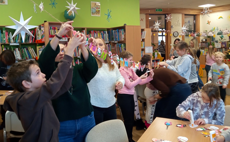 Grupa osób złożona z dzieci i dorosłych zakłada ozdoby na sznurku