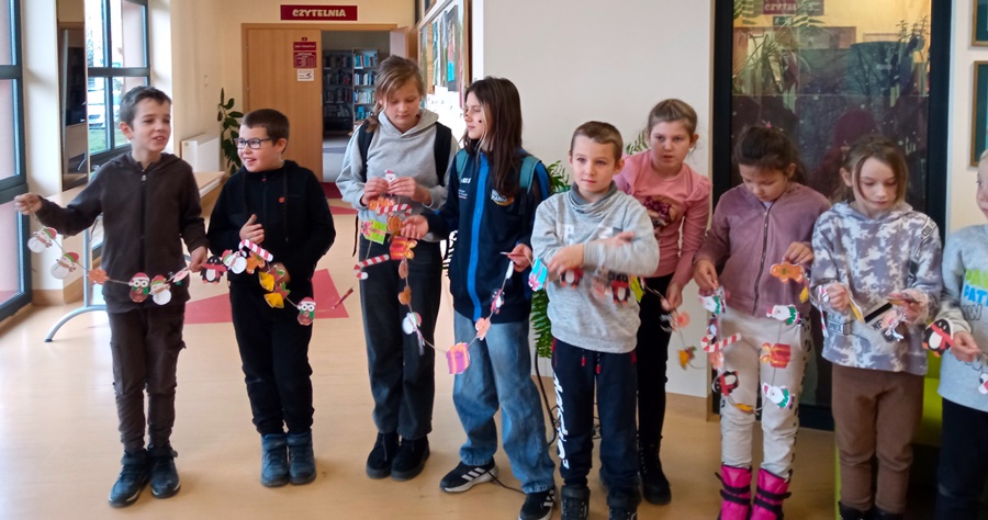 Kilkoro uczniów stoi na korytarzy a w rękach trzymają łańcuch z ozdobami swiątecznymi