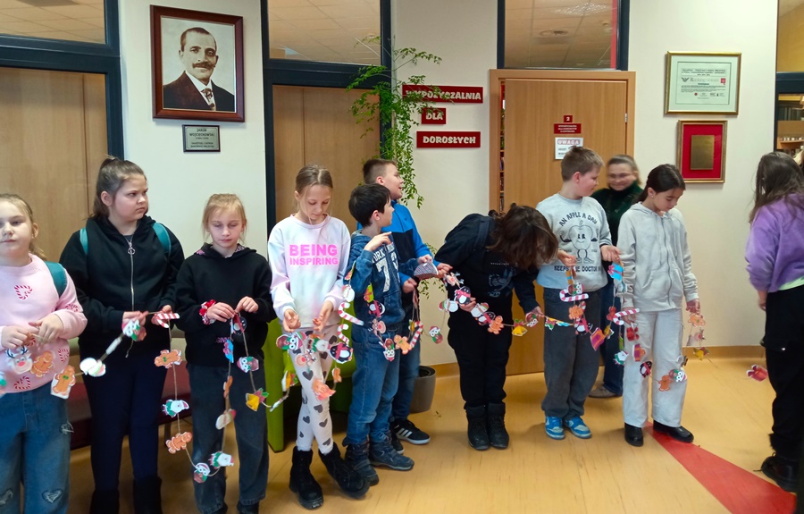 Kilkoro uczniów stoi na korytarzy a w rękach trzymają łańcuch z ozdobami swiątecznymi