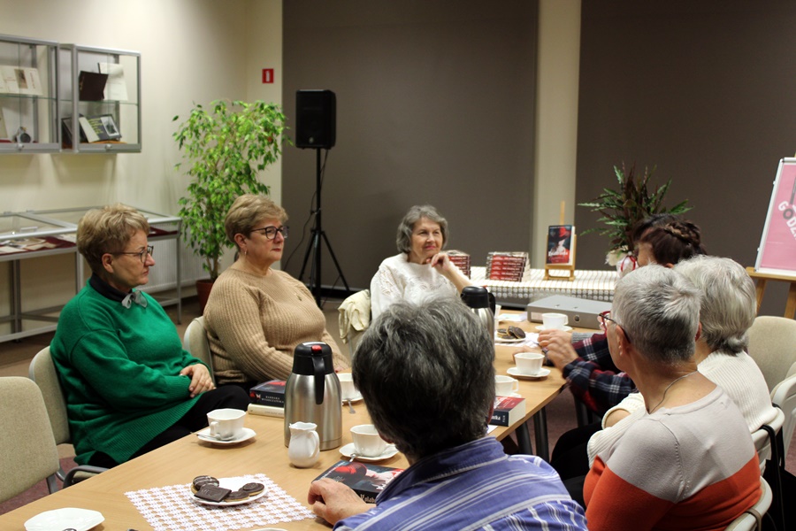 Osoby obecne na spotkaniu siedzą przy stole i dyskutują o przeczytanej książce.