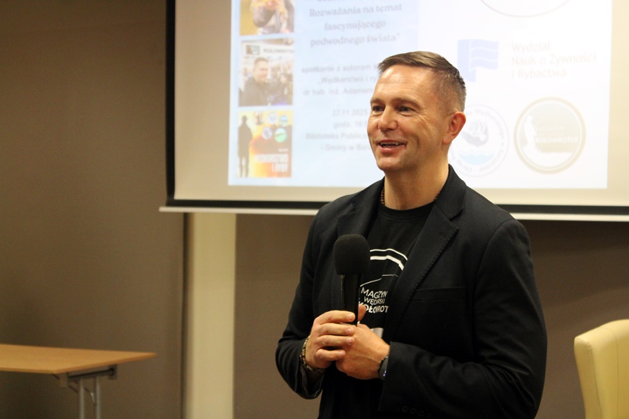 Pan Adam Tański stojący z uśmiechem przed publicznością.