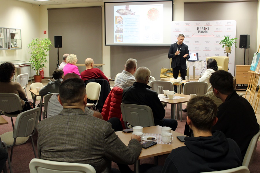 Zdjęcie z tyłu sali pokazujące publiczność i zaproszonego gościa.