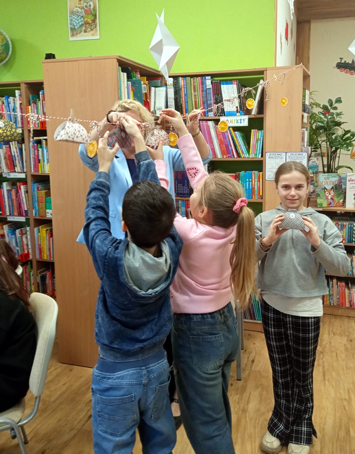 Bibliotekarka i dwójka dzieci mocuje ozdoby na sznurku, jedna z
