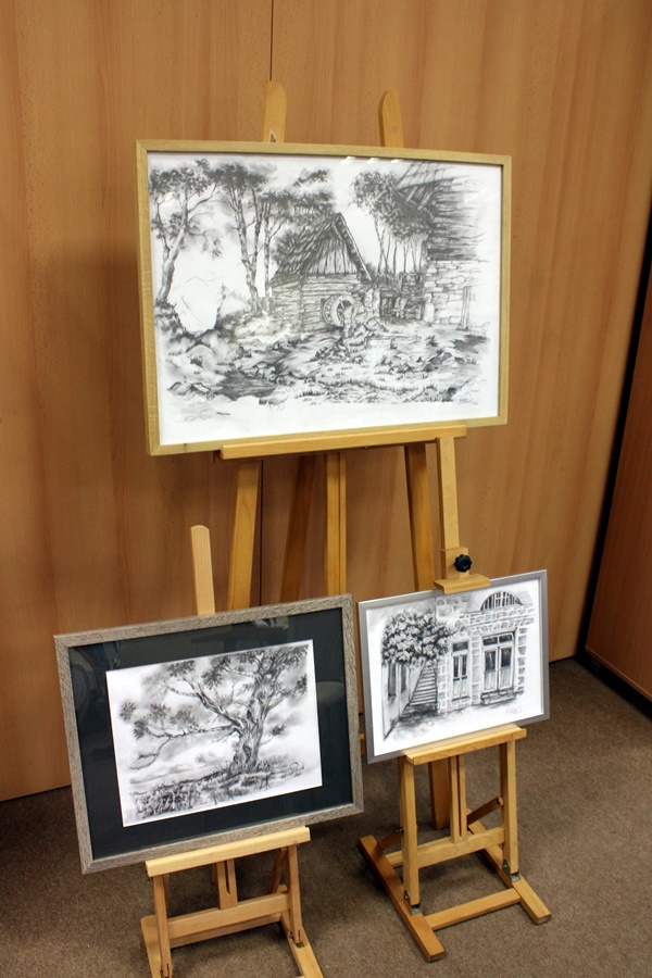 Trzy czarno-białe obrazy wystawione na wernisażu, jeden większy stojący na dużej sztaludze dwa mniejsze stoją pod nim na małych sztalugach