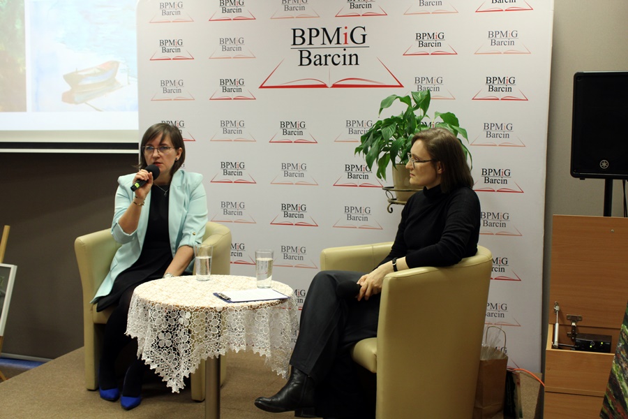 Prowadząca spotkanie bibliotekarka i zaproszona artystka siedzą w fotelach na scenie i rozmawiają między sobą