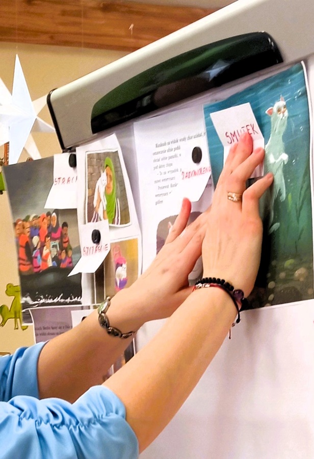 kobiece dłonie trzymające przy tablicy kolorowy arkusz papieru