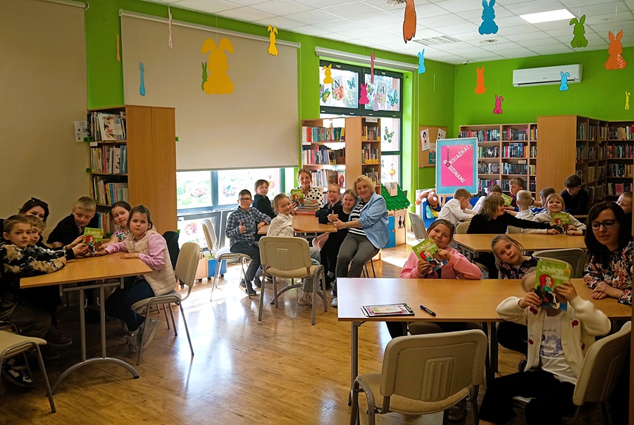 Dzieci i bibliotekarka siedzą przy stołach