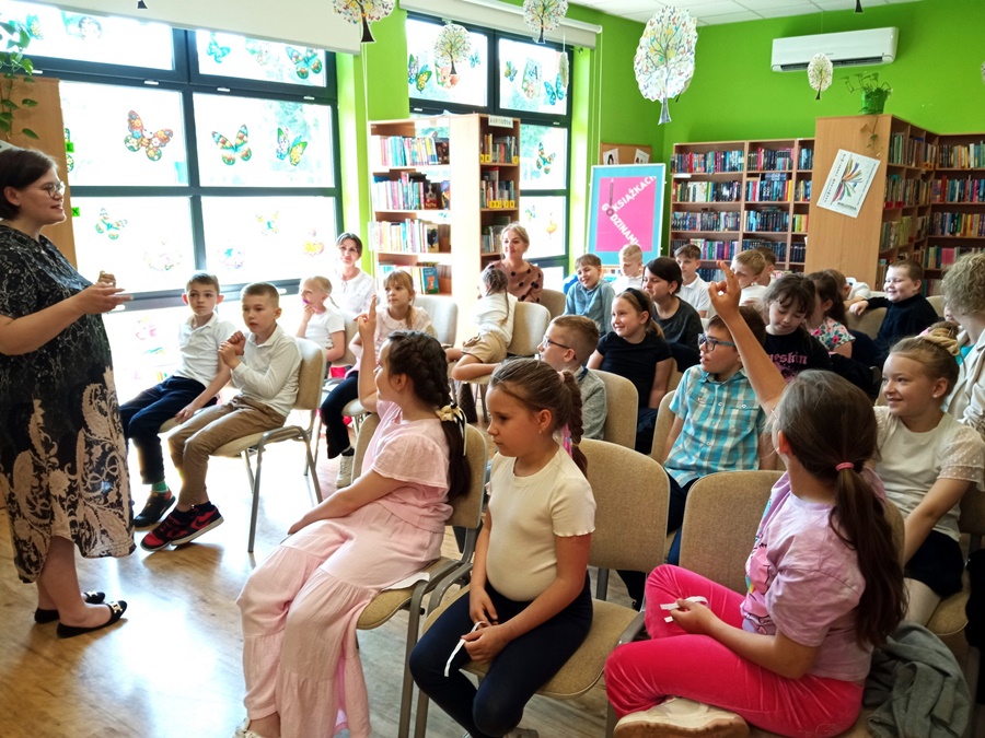 Dzieci siedzą na krzesłach i słuchają zaproszonej autorki