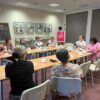 Uczestniczki spotkania i zaproszona bibliotekarka siedzą przy stołach i rozmawiają o ksiażkach.