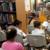 Bibliotekarka pokazuje jednemu z dzieci zawartość książki o której opowiada.