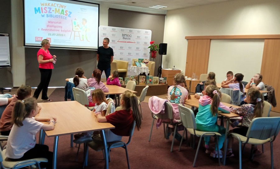 Ilutrator stoi przed zebranymi na zajęciach dziećmi i tlumaczy im co będą dzisiaj robić