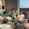 Pani Renata Bożek stoi przy mównicy i wygłasza swój referat o Jakubie wojciechowskim.